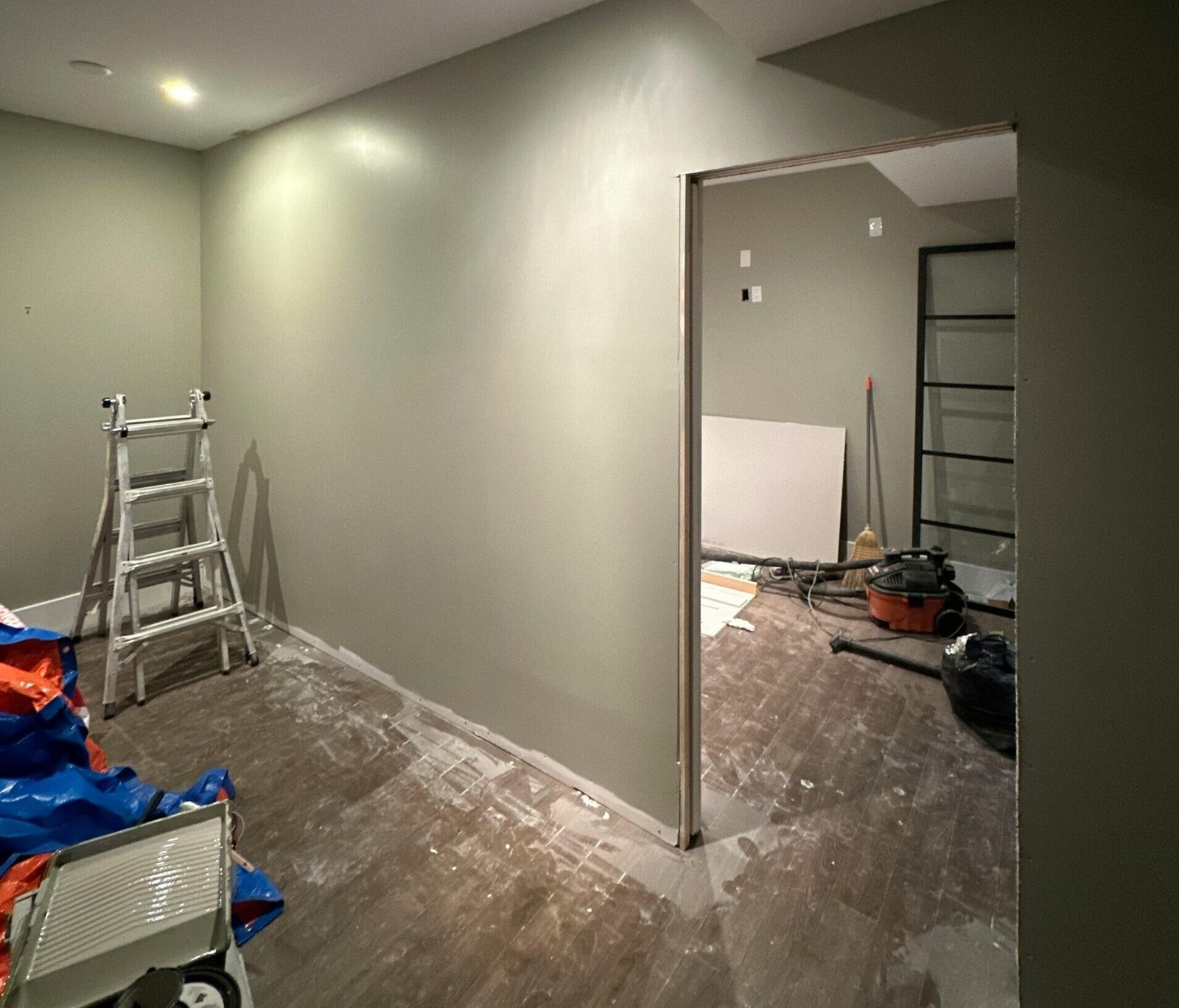Interior view of a room under renovation, featuring a ladder and tools on the wooden floor.